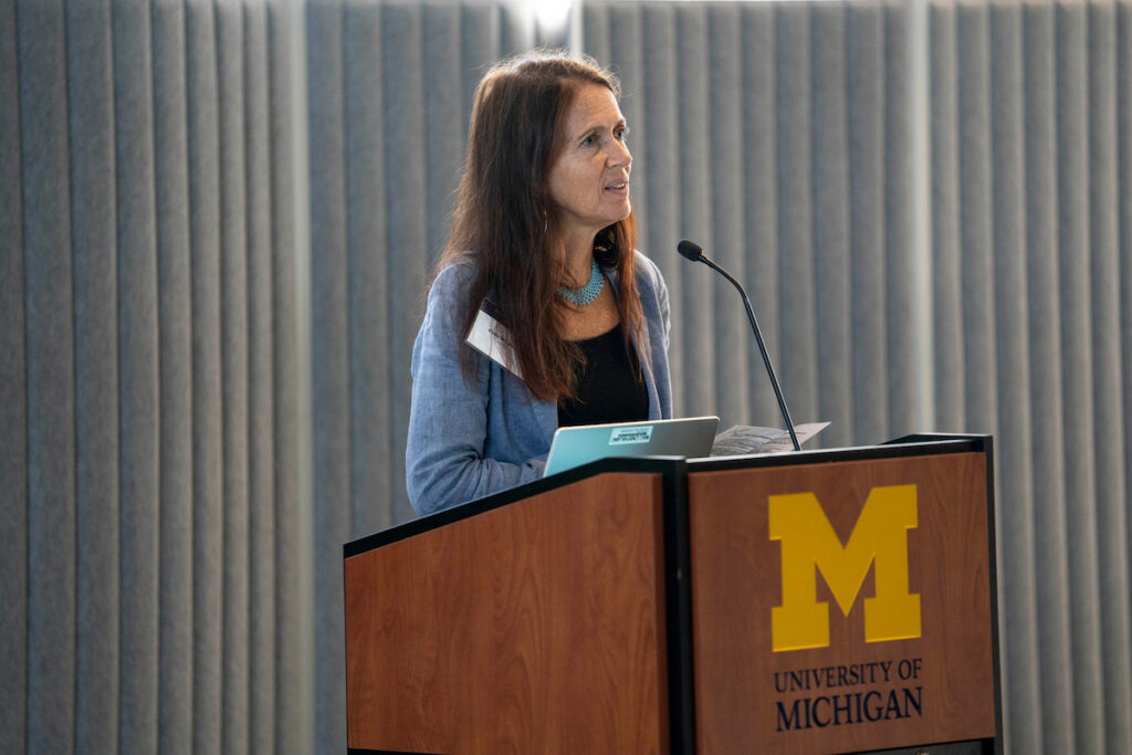 A person speaks at a podium bearing the University of Michigan logo during a presentation.