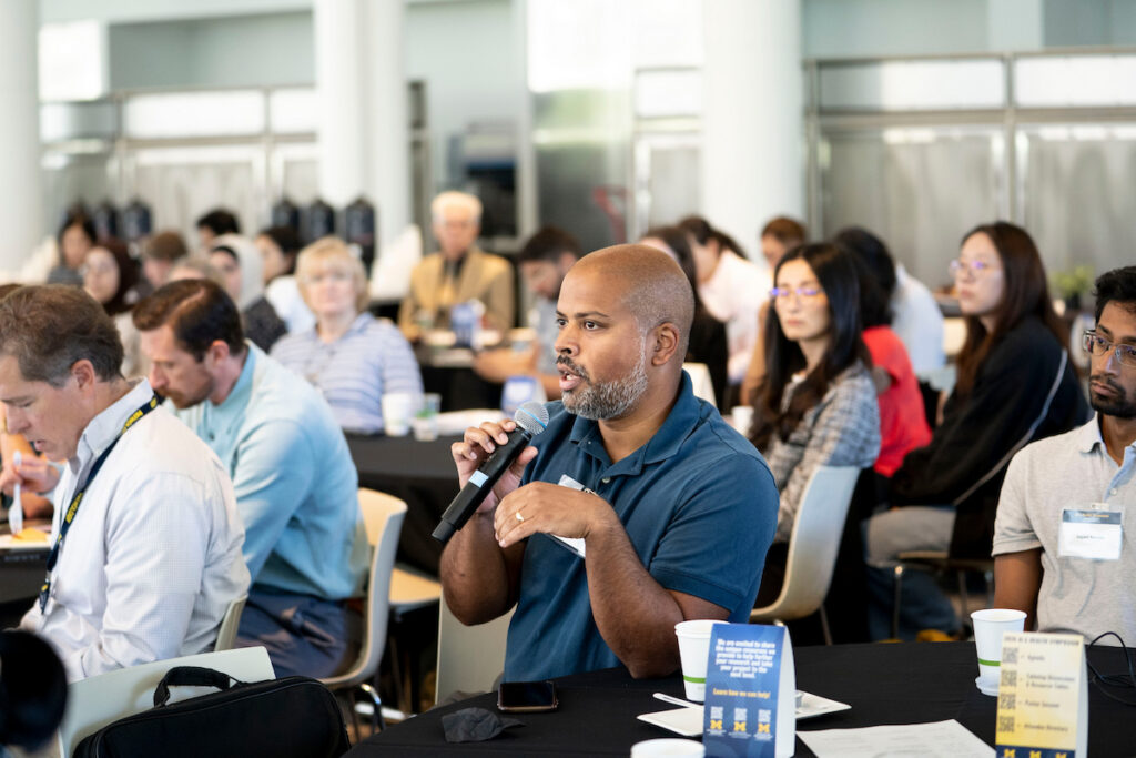 A person speaks into a microphone at a conference table while others listen attentively in a conference room setting.
