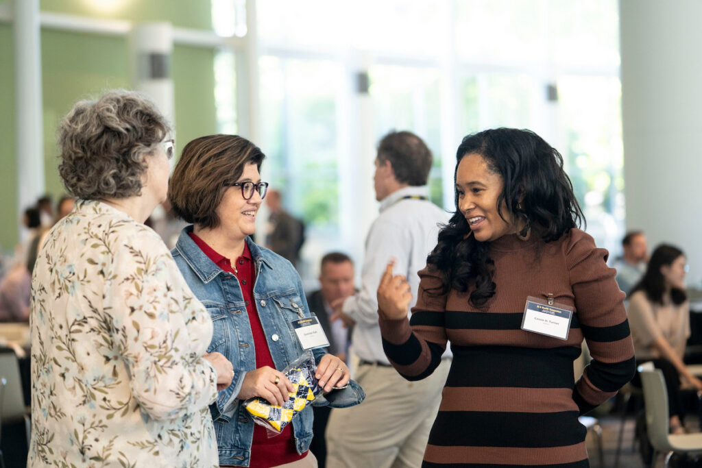 Three individuals engage in a lively conversation at a social gathering, with one person gesturing animatedly while others listen attentively.