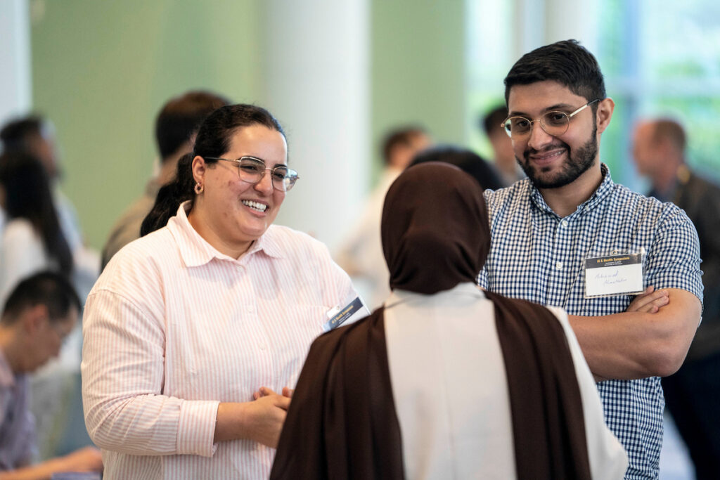 Three people engage in friendly conversation at an event, with one smiling warmly while another listens attentively.