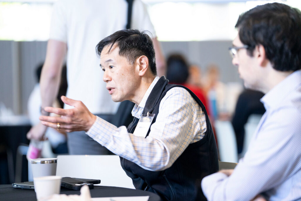 Two individuals engage in conversation at a conference table, with one gesturing while speaking.