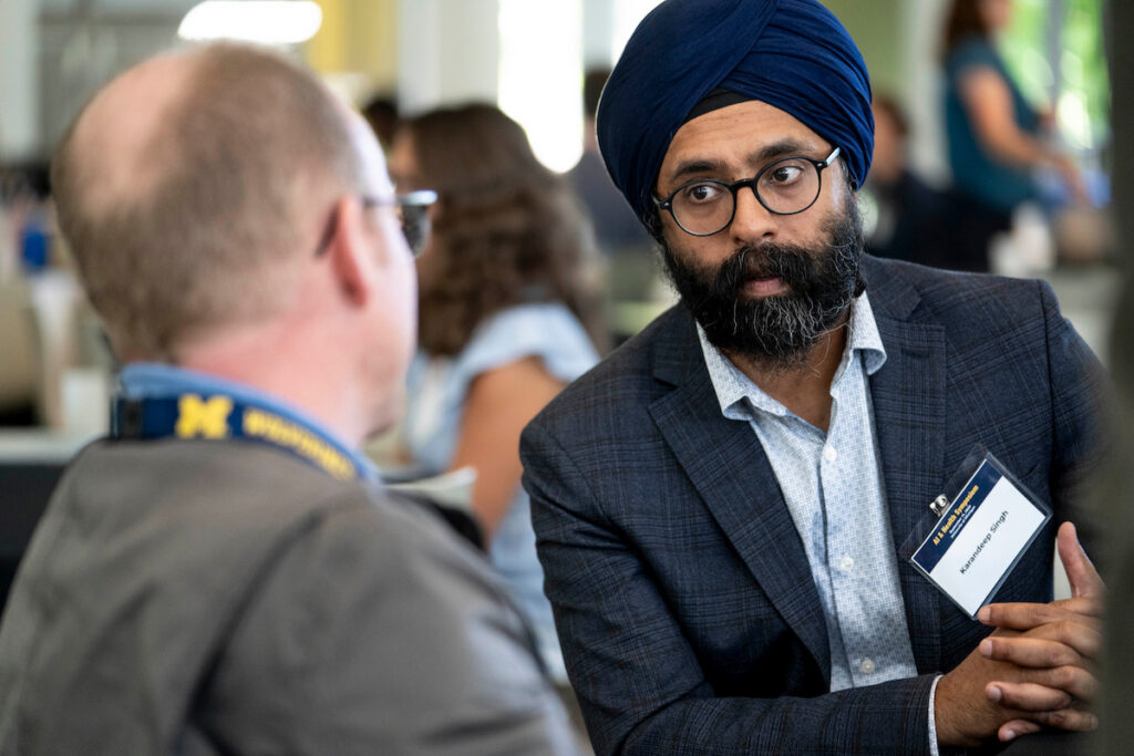 A person wearing a blue turban and glasses engages in conversation with another individual at what appears to be a professional event.