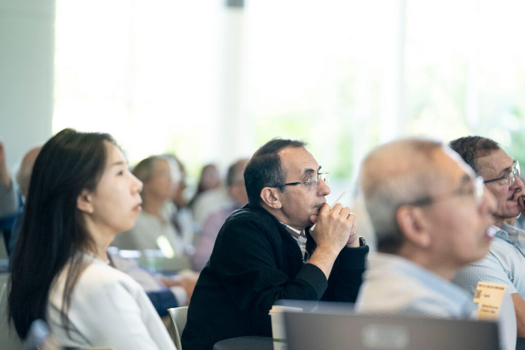 A group of attendees at a conference or seminar are seated, attentively listening to a presentation.