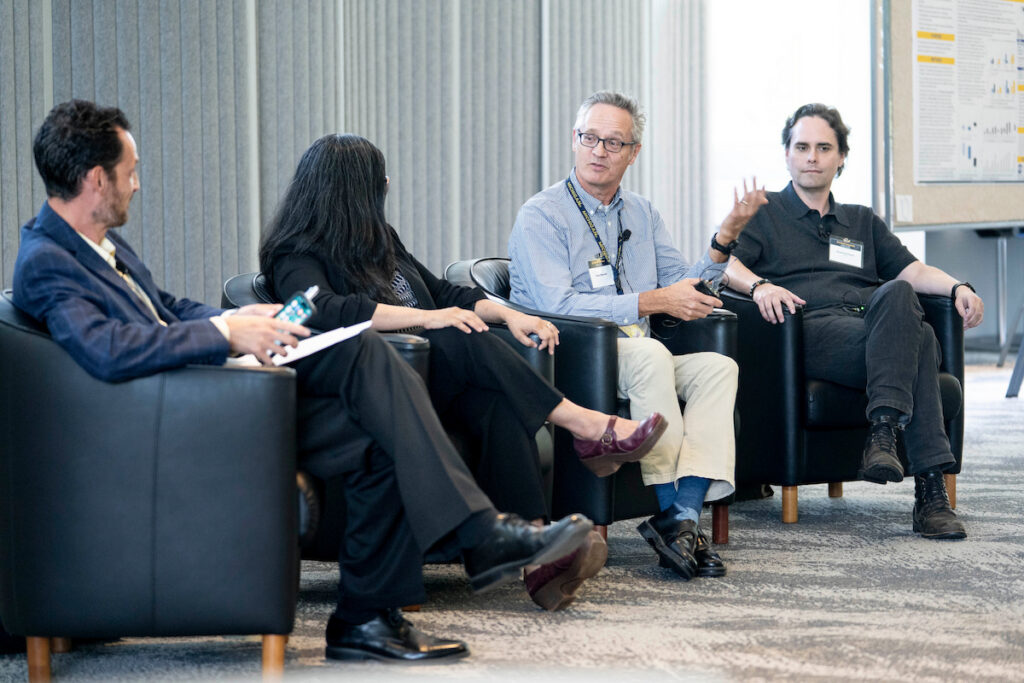 Four individuals are seated in black armchairs during a discussion in a modern, well-lit room.