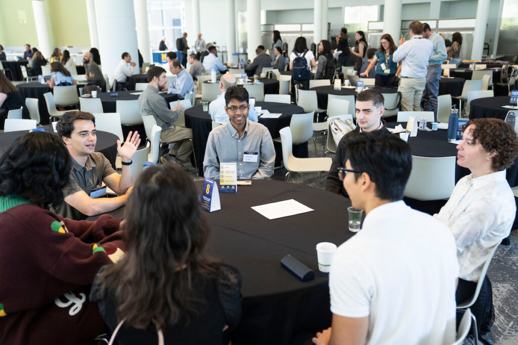 A group of people are engaged in conversation around a round table at a conference or networking event.