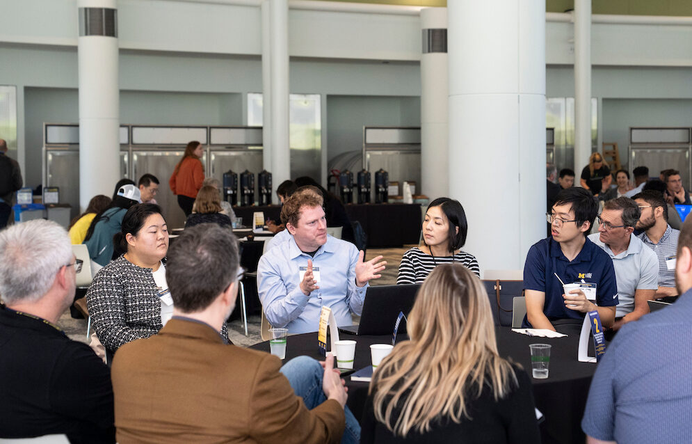 A group of people are engaged in conversation around a table at an indoor event.