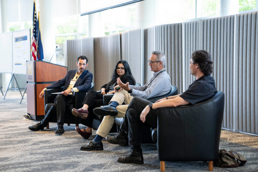 Four individuals are seated in a modern conference room, engaged in a discussion during a panel event.